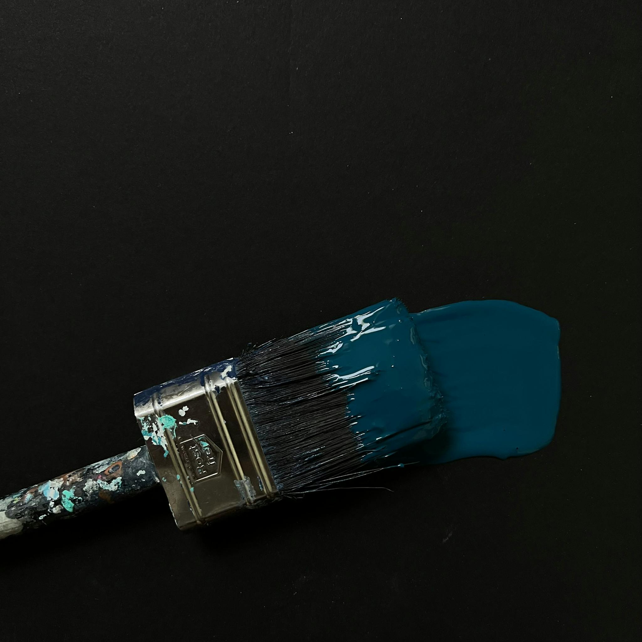 A close-up image of a paintbrush laying down a stroke of blue paint on a dark background.