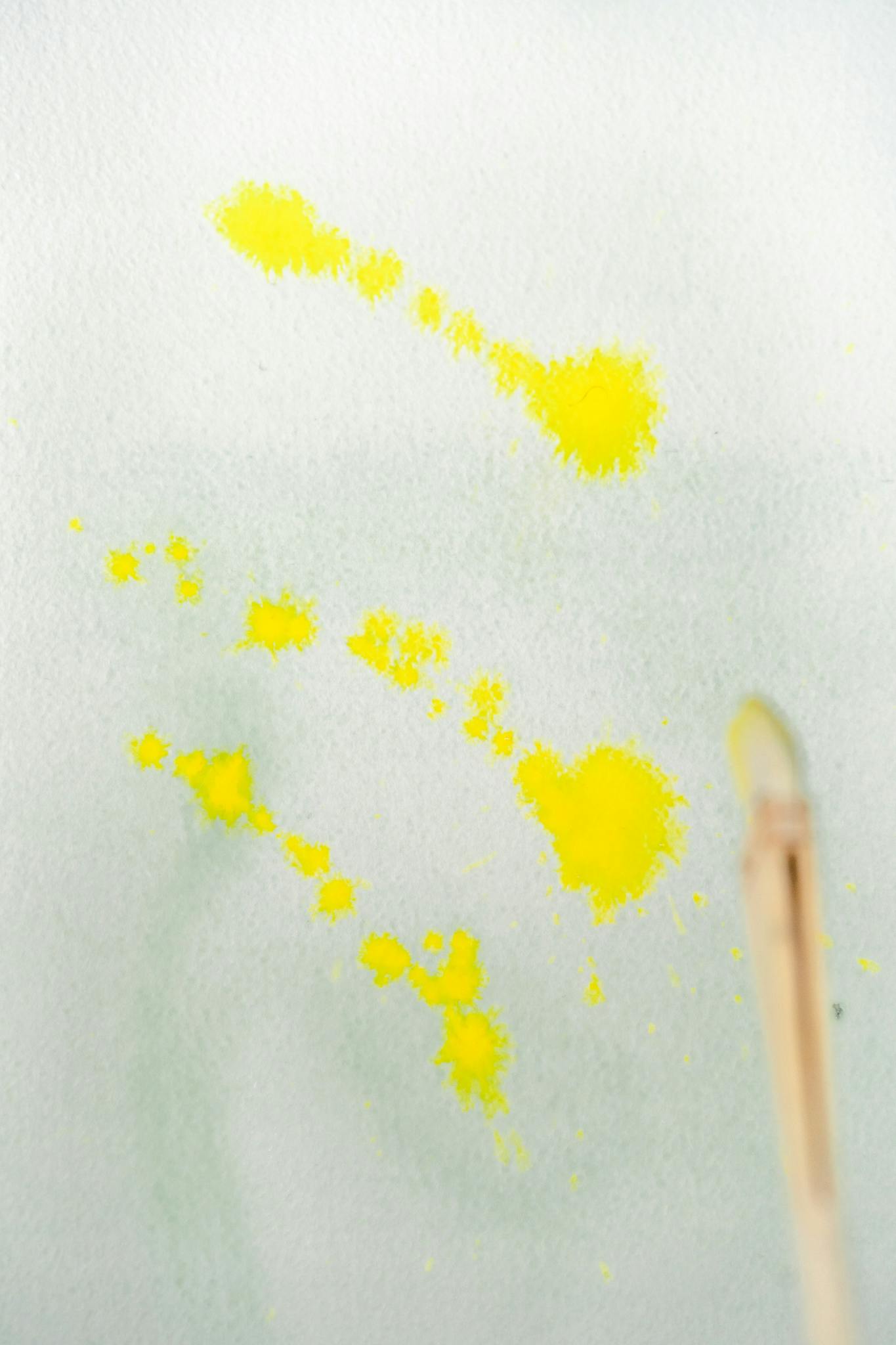 Dynamic macro shot of yellow watercolor splashes with paintbrush on paper.
